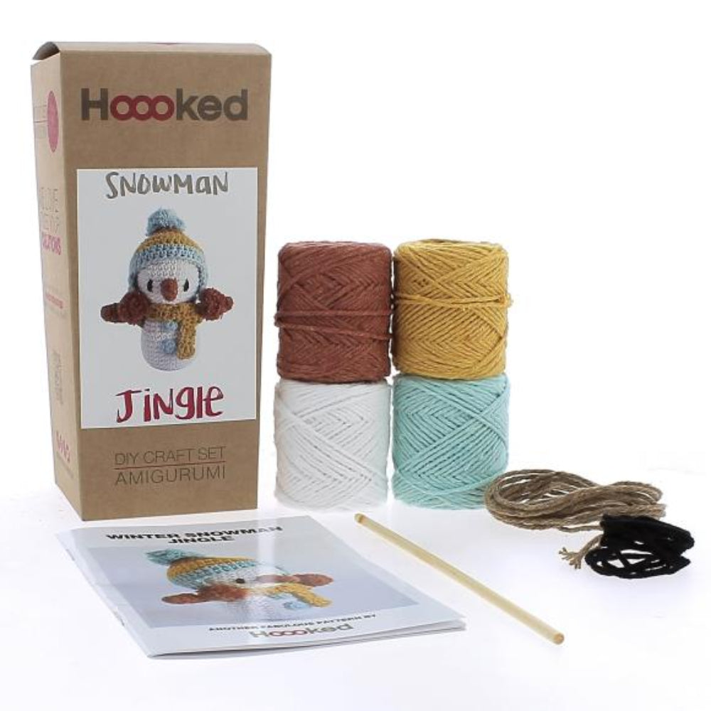 Crochet kit with yarn in brown, yellow, white and blue, hook, and instructions for a snowman crochet project on a white background.