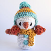 A crocheted snowman toy with a colorful hat and scarf on a white background