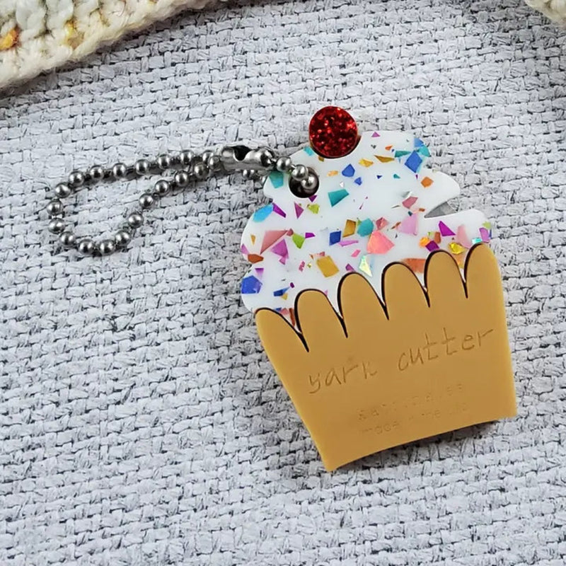 Cupcake shaped thread cutter keychain with colorful sprinkles on a woven surface