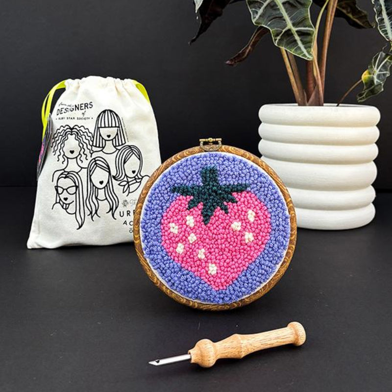 Embroidery hoop with strawberry design, white drawstring bag, and plant on dark background