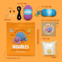 Wobbles yarn kit packaging with yarn, needles, and instructions on an orange background