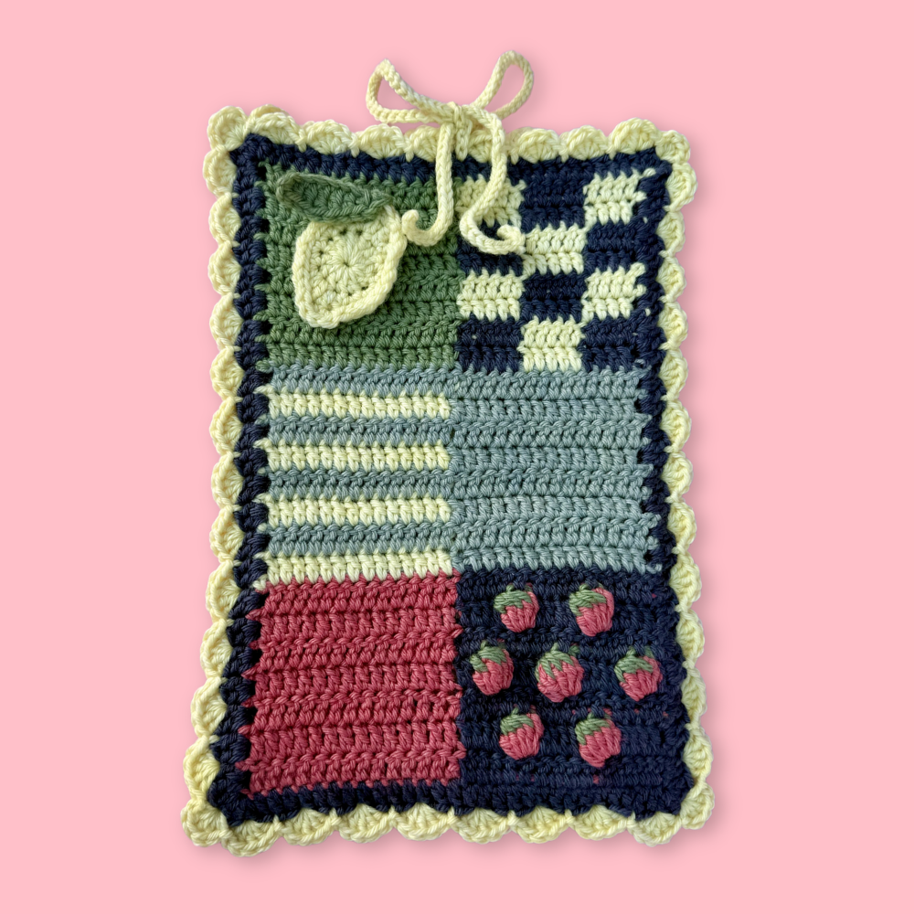Crocheted book sleeve with patchwork pattern on a pink background