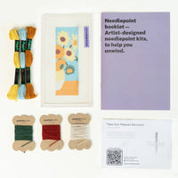 Needlepoint kit with floss, needle, and a floral design on a white background
