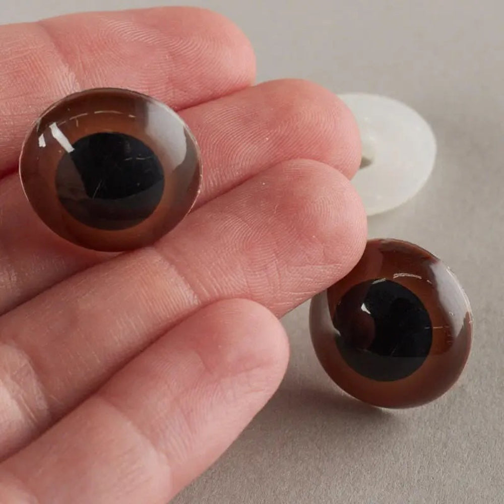 Two brown glass eyes held between fingers on a neutral background