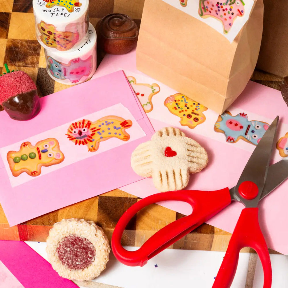 Decorative cookies with animal cookie designs on the washi tape, colorful paper, and red scissors on a wooden surface.