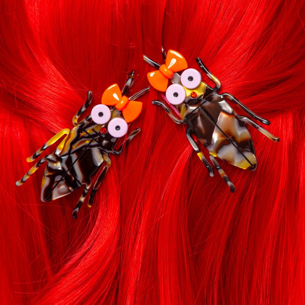 Two decorative hair clips shaped like cockroaches on red hair.