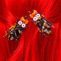 Two decorative hair clips shaped like cockroaches on red hair.