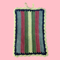 Striped crocheted book sleeve with green, pink, and blue colors on a pink background
