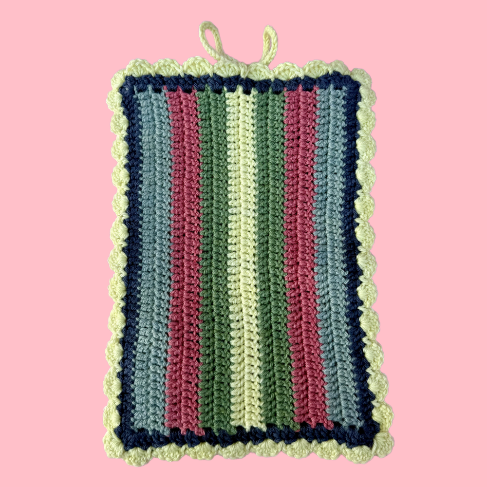 Striped crocheted book sleeve with green, pink, and blue colors on a pink background