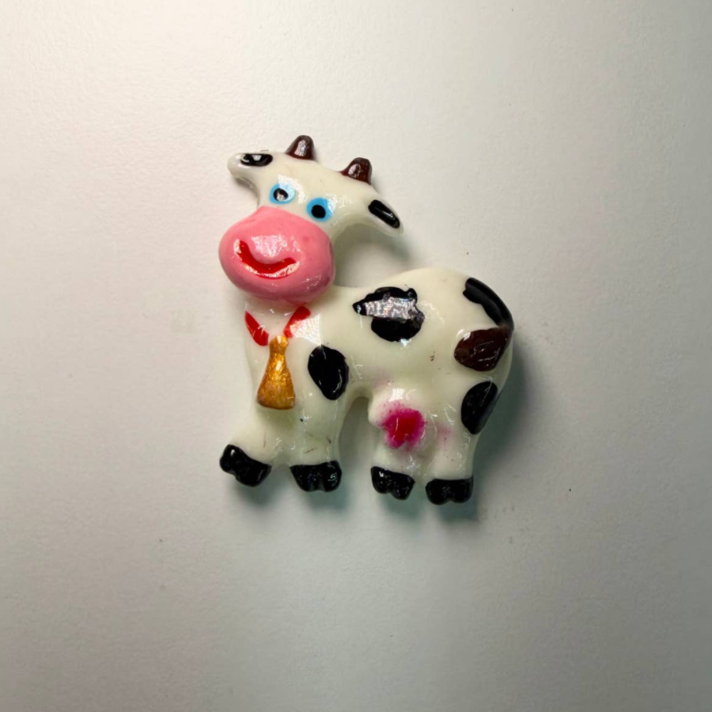 Small cow magnet with blue eyes, a pink nose and a gold bell around its neck