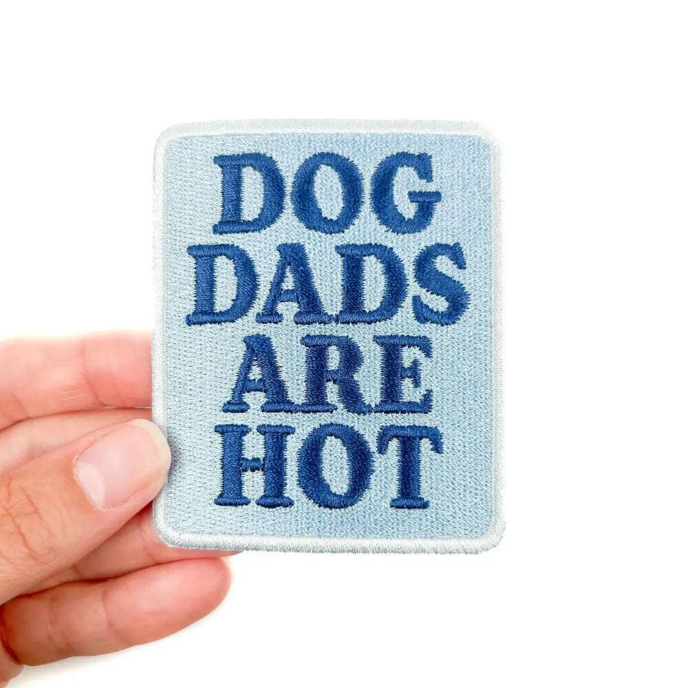 Embroidered patch with 'DOG DADS ARE HOT' text held by a hand on a white background