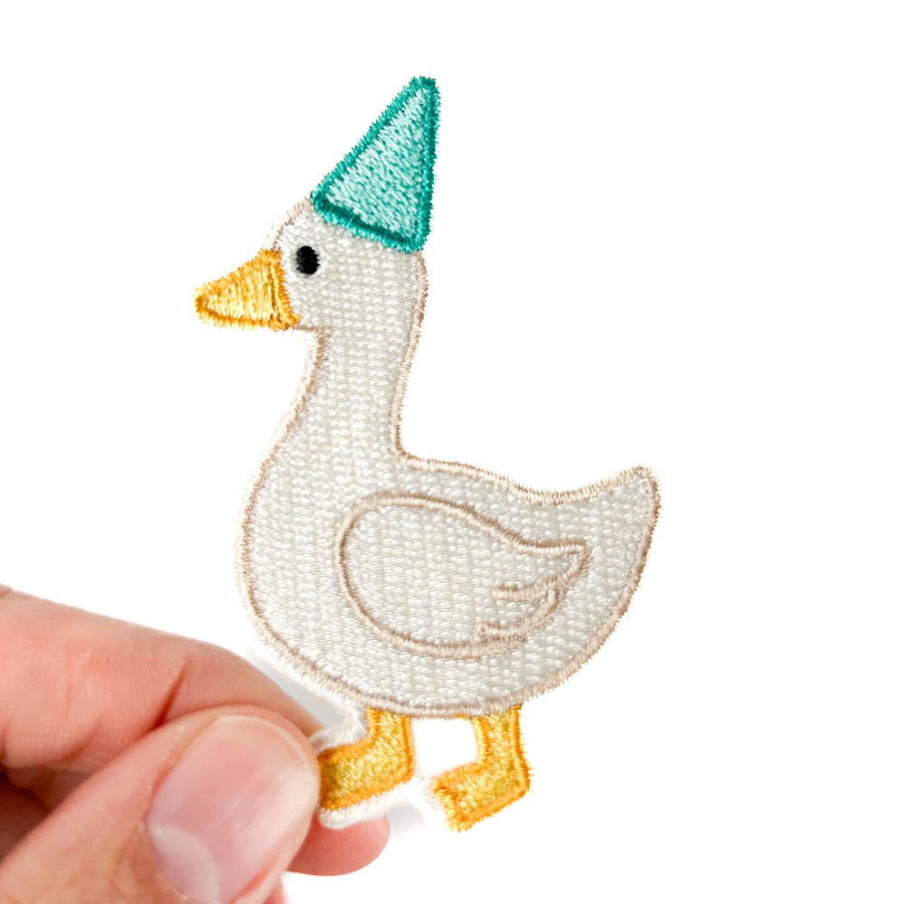 Embroidered patch of a goose wearing a green hat held by a hand on a white background