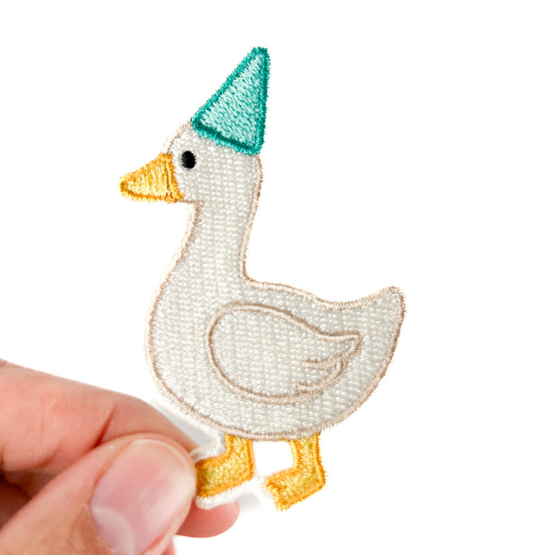 Embroidered patch of a goose wearing a green hat held by a hand on a white background
