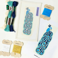 Needlepoint kit with peacock design, threads, and tools on a white background