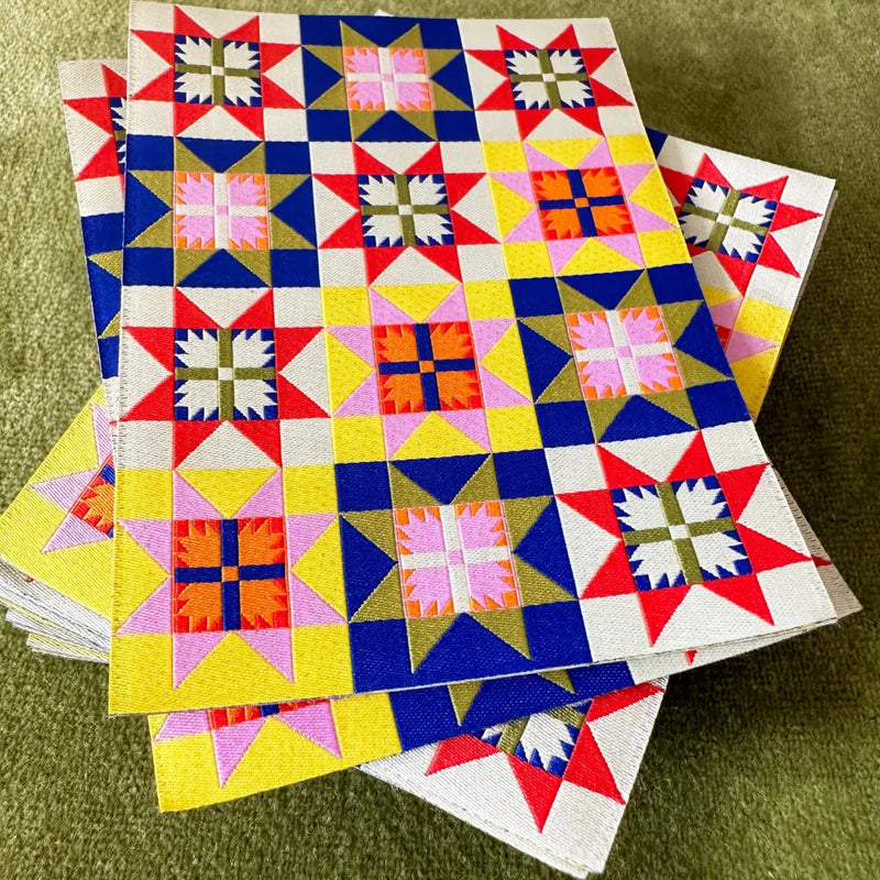Stack of colorful quilt-style sticker patches with a pink information card on a green background. 