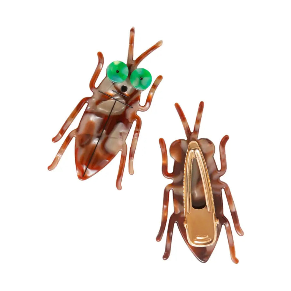 Two cockroach-shaped hair clips with green eyes on a white background