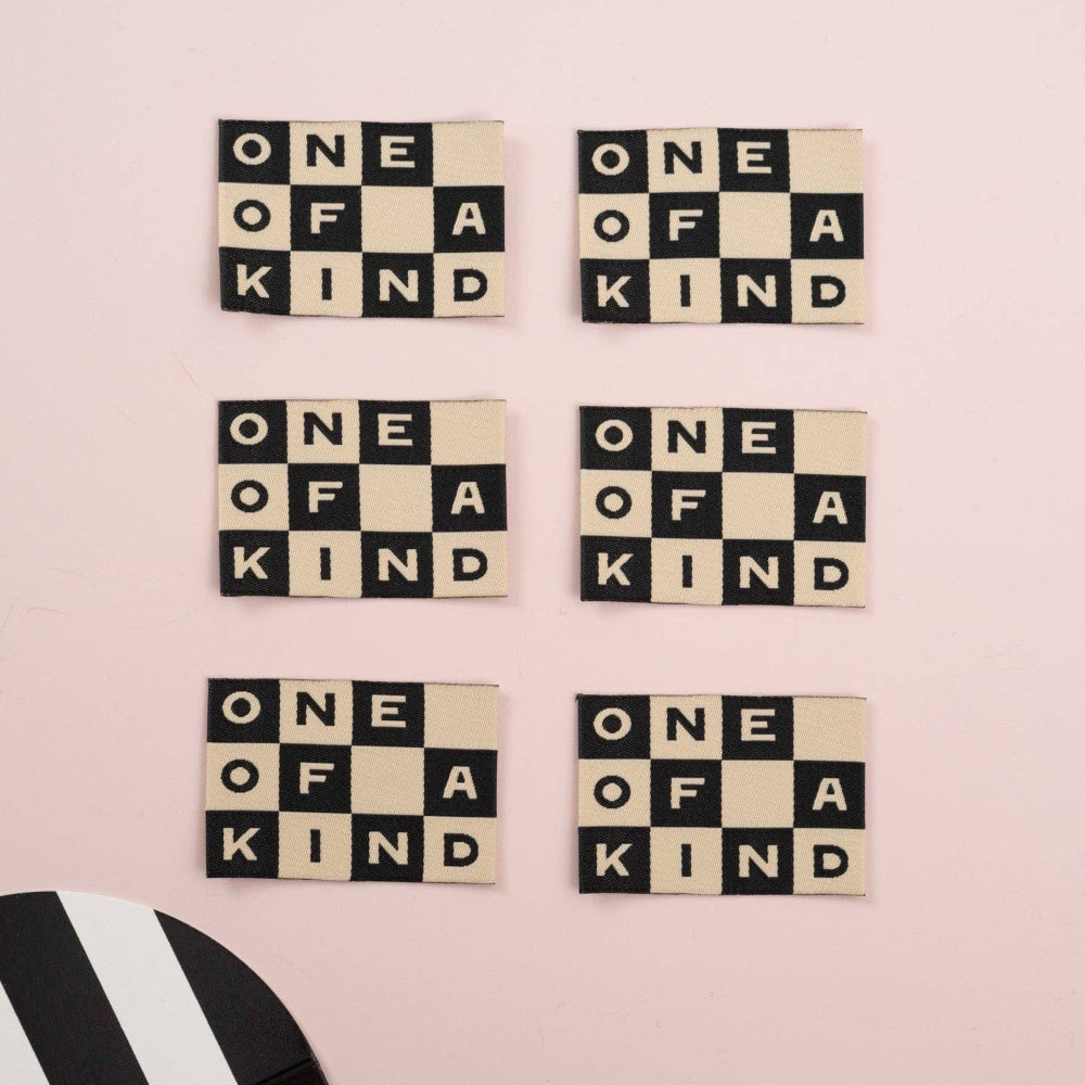 Set of letter tiles with 'One of a Kind' text on a pink background, with a card partially visible.