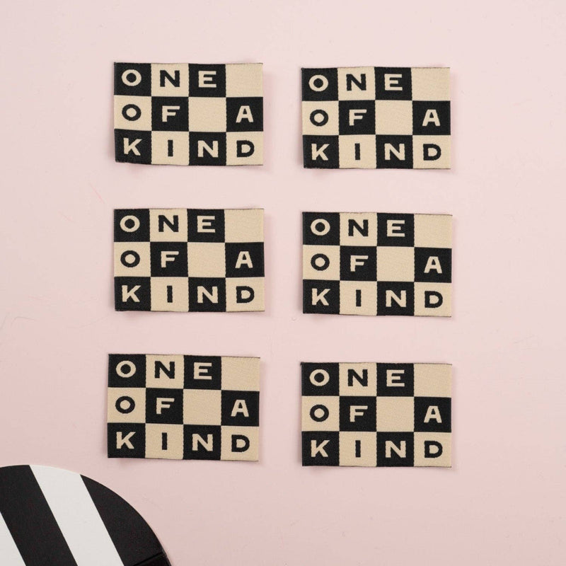 Set of letter tiles with 'One of a Kind' text on a pink background, with a card partially visible.