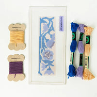 Needlepoint kit with thread spools and fabric on a white background
