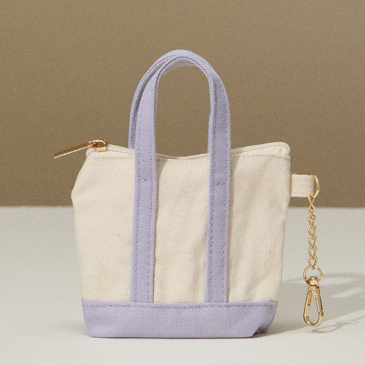 Mini tote bag with lavender bottom and handles, zip top, and key chain on the side.