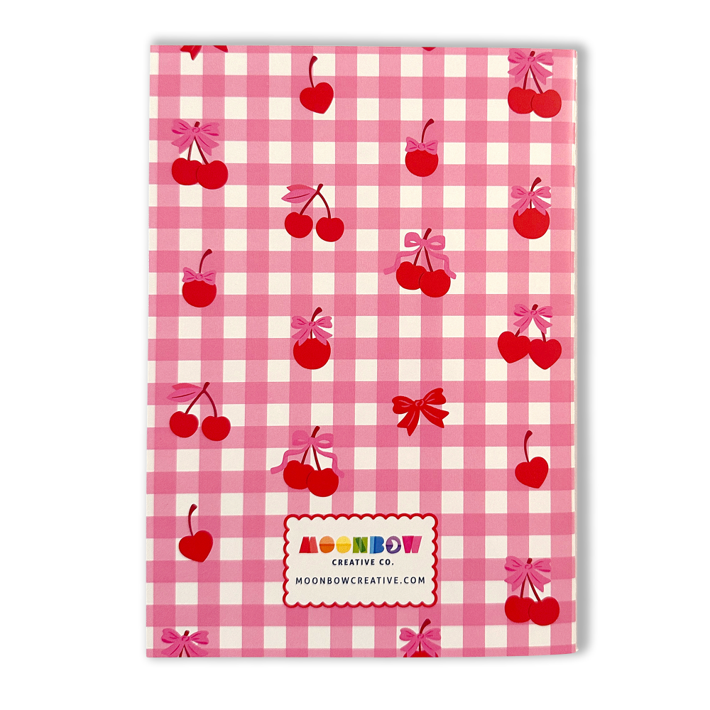 Notebook with pink gingham pattern, red cherries, and bows on a white background. Brand 'Moonbow Creative Co.' visible.