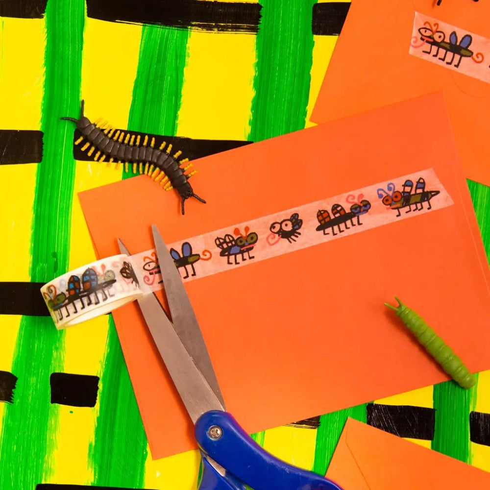 Orange paper with bugs washi tape, scissors, and a centipede on a colorful striped background.