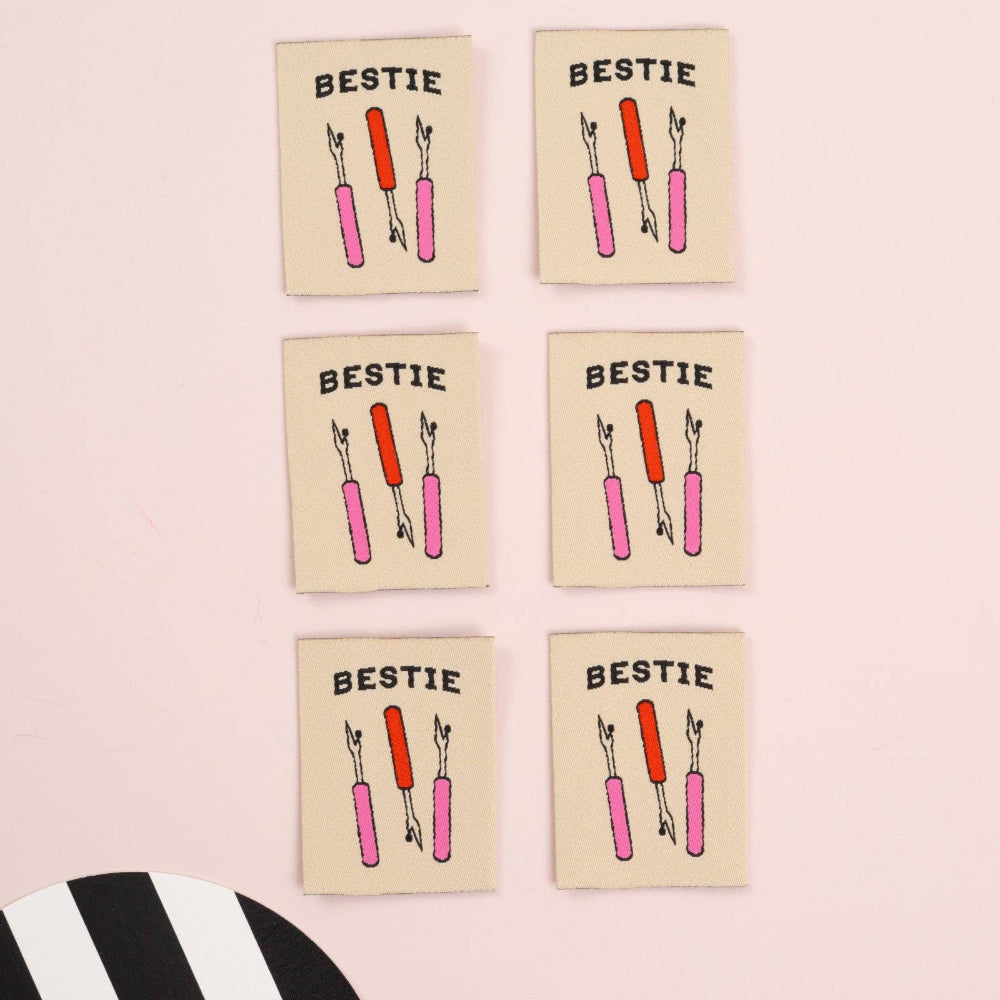 Six 'Bestie' labels with three seam rippers on a pink background