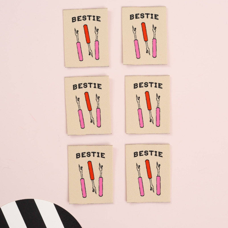 Six 'Bestie' labels with three seam rippers on a pink background