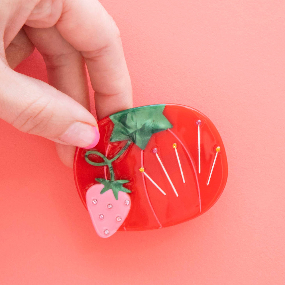 Tomato-shaped pincushion with pins hair claw on a pink background