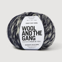 A ball of dark blue and white variegated yarn with a white paper label that reads 'WOOL AND THE GANG' on a light gray background.
