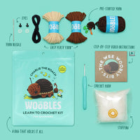 Wobles learn to crochet kit with yarn, hook, and other supplies on a teal background