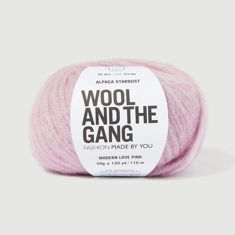 A ball of Wool and the Gang's Alpaca Stardust yarn in Modern Love Pink, featuring a white paper label with black text, set against a clean, light gray background.