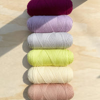 yarn skeins in a purple and yellow color scheme against a wooden surface. 