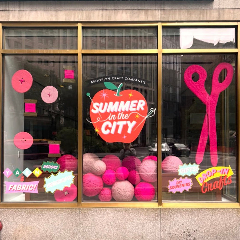 Store window display with 'Summer in the City' theme featuring pink and red decorations.