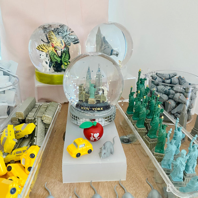 Collection of small models and toys including a New York-themed snow globe, toy cars, and miniature buildings.
