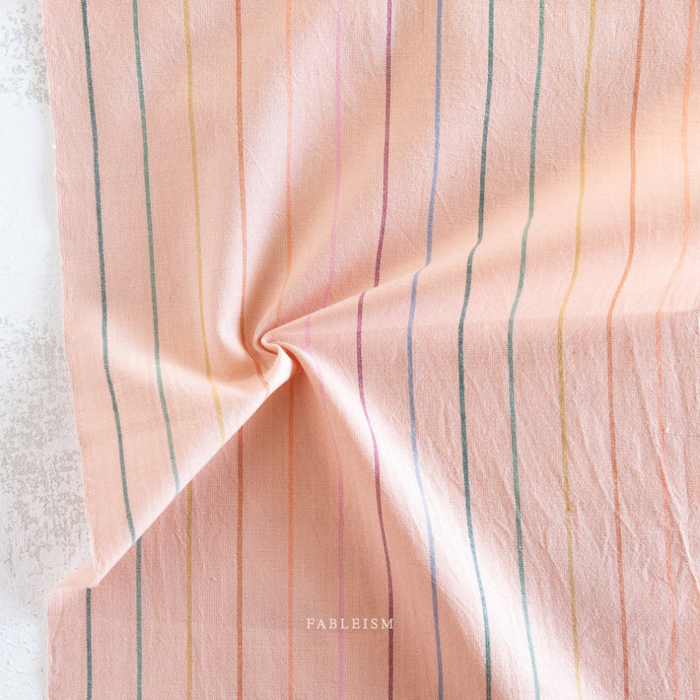 Pink fabric with multicolored stripes on a textured surface, featuring the brand 'Fableism'.