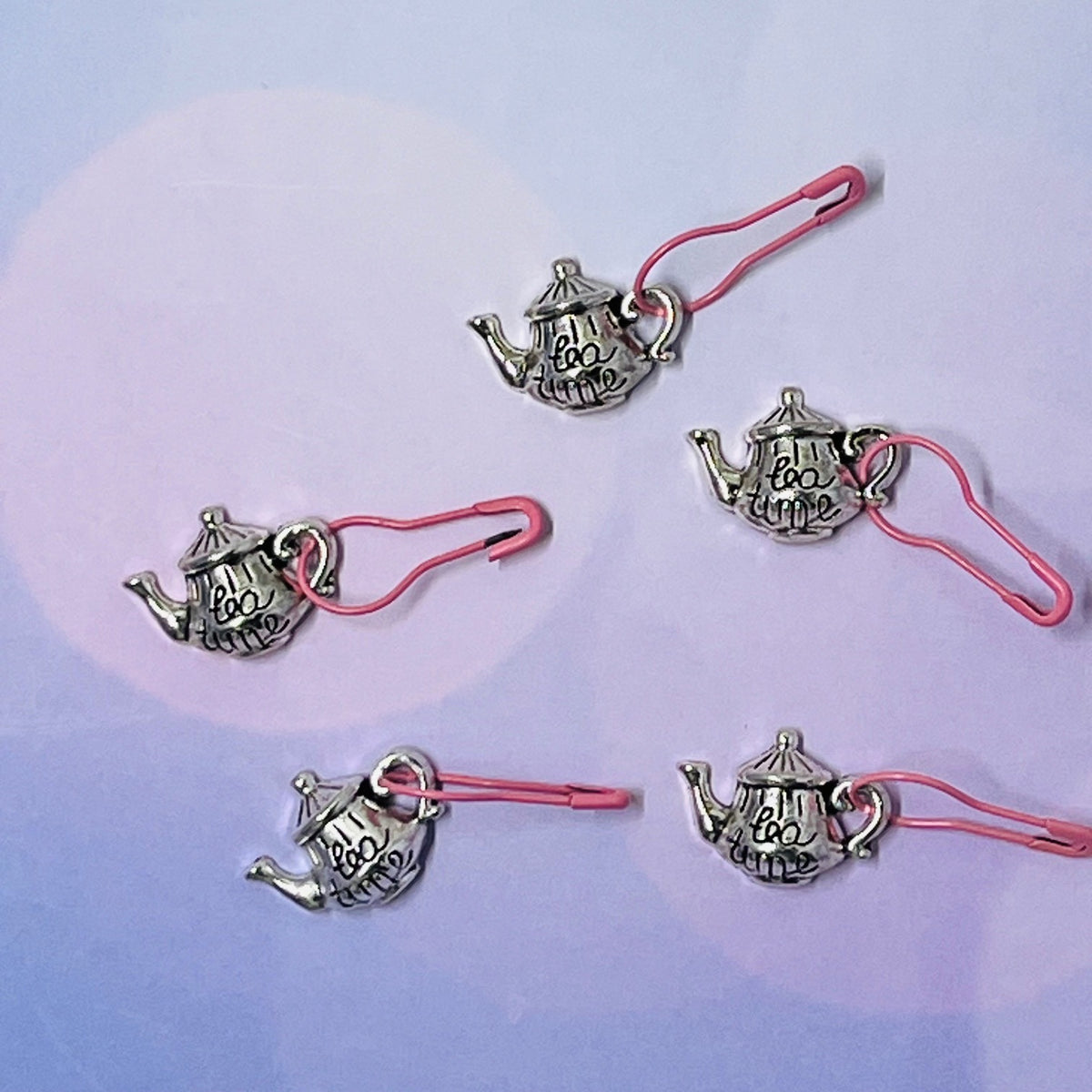 Silver metal teapot-shaped markers with tea time written on them in cursive with a pink pin.