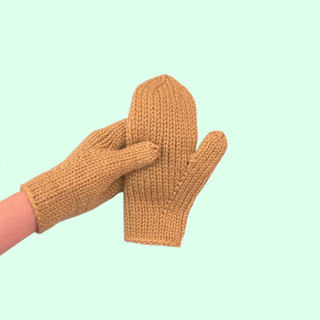 Hand wearing a knit mitten holding another knit mitten on a blue background.