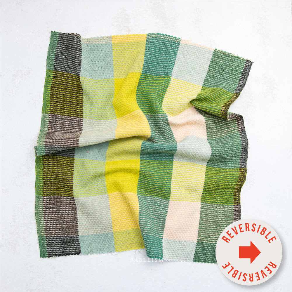 Textured fabric swatch in green, blue, and yellow. Sticker says "reversible" in front