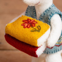 Stuffed animal holding a yellow book with a red flower design on a blurred background