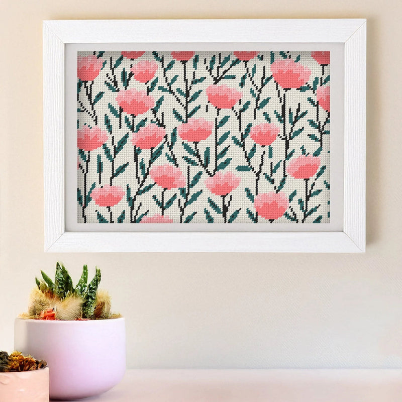 Framed needlepoint artwork with a floral design on a tan wall