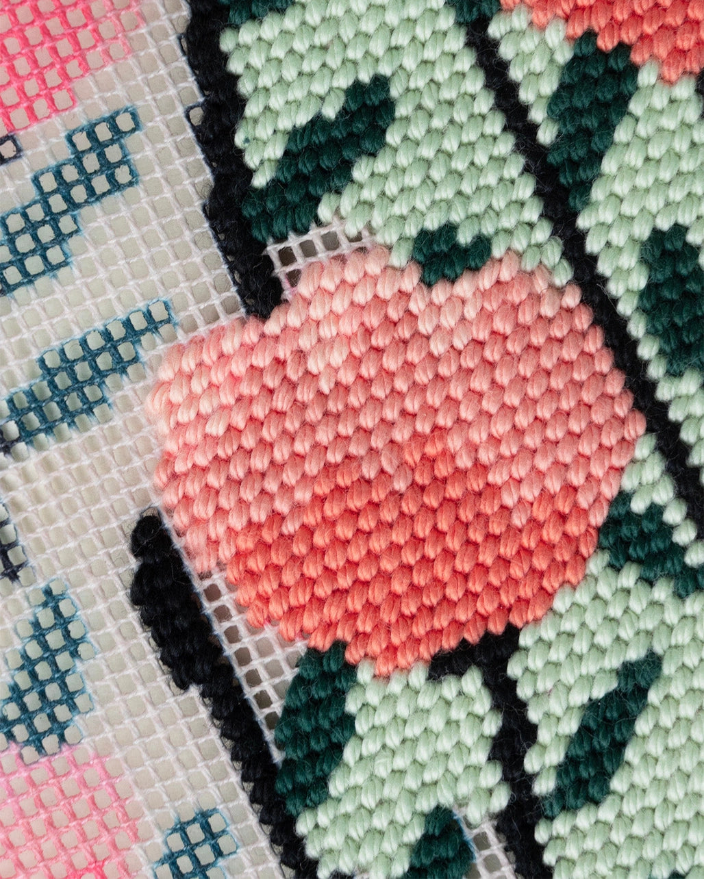 Close-up of a needlepoint canvas with a pink and green flower design