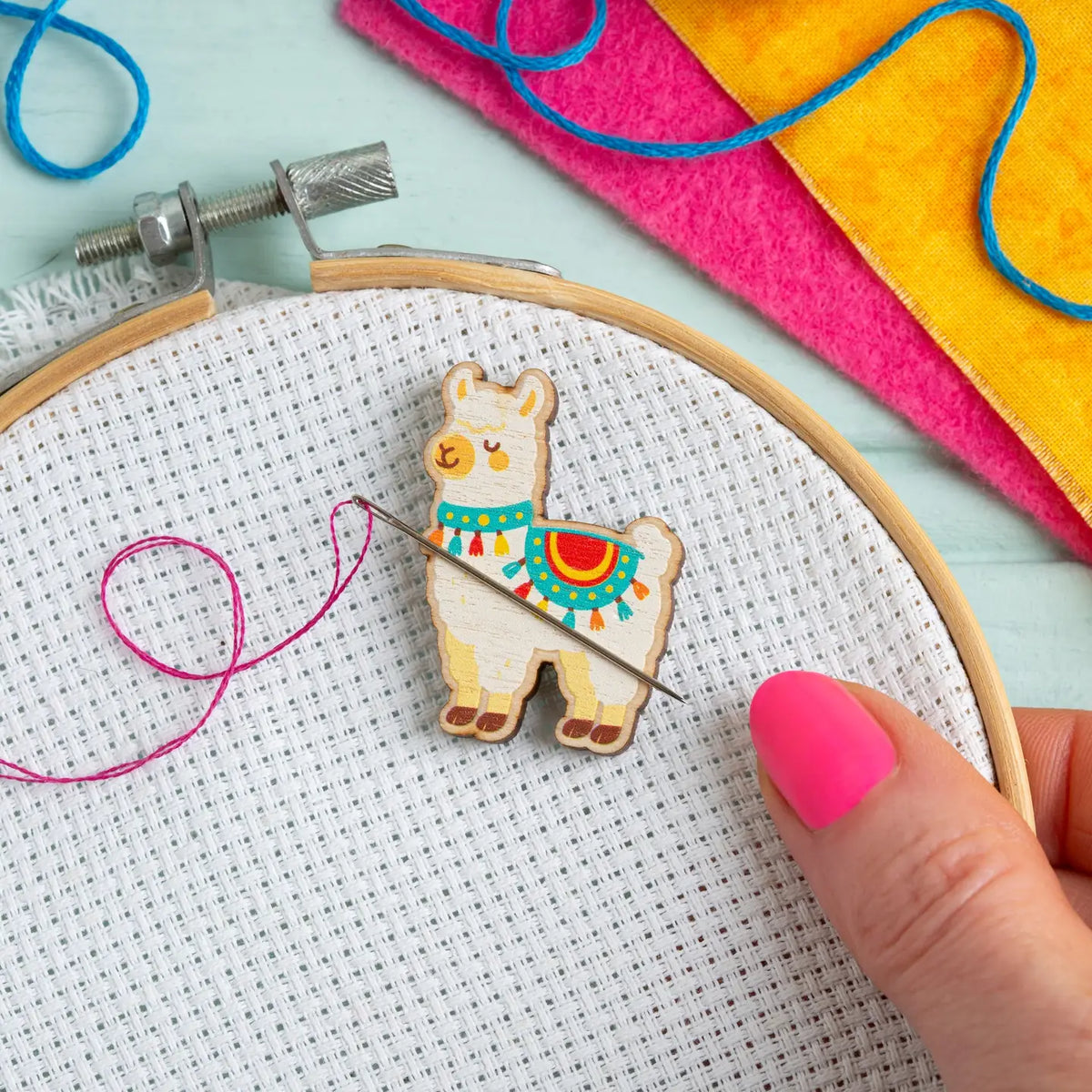 Embroidery hoop with an alpaca needle minder and colorful threads on a light blue background
