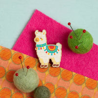 Colorful alpaca-shaped needle minder on a pink and orange fabric background with green felt balls with pins in them