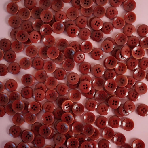 A collection of amber-colored corozo nut buttons with four holes, displayed on a surface.