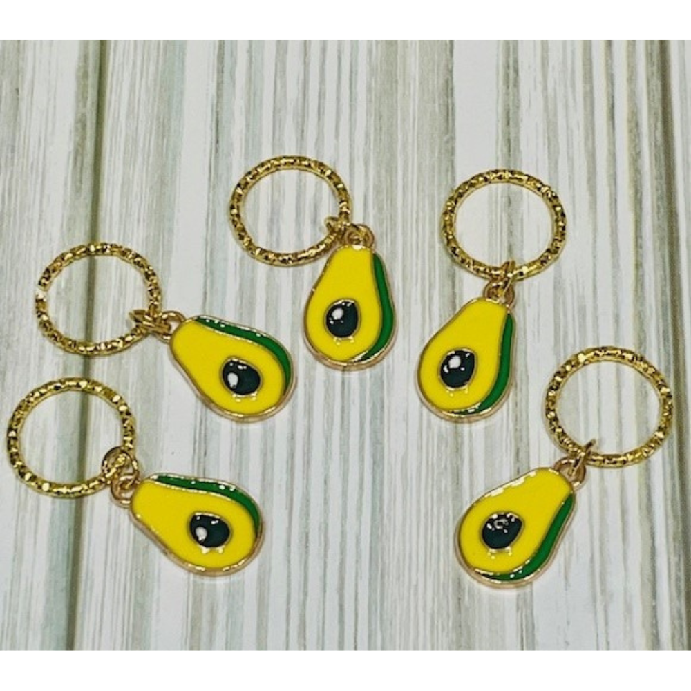 Avocado-shaped charms with gold loops on a wooden surface