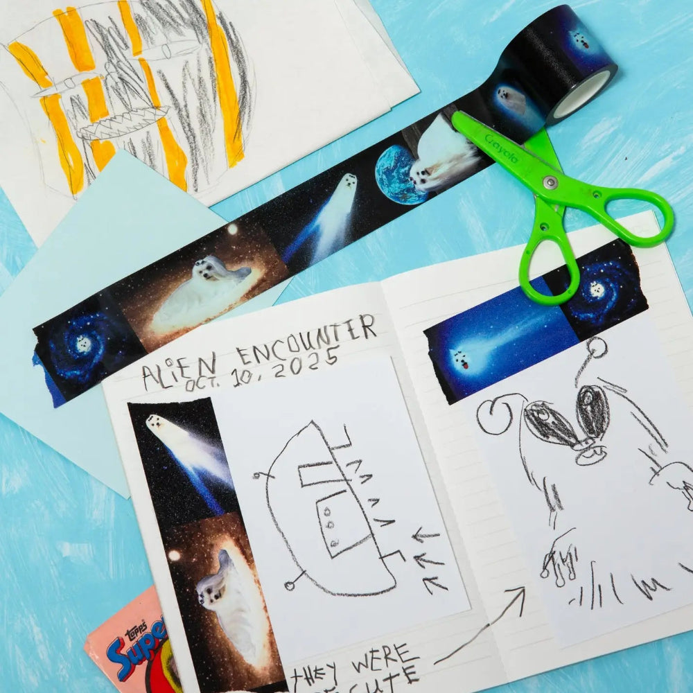 Children's drawings of aliens and space-themed tape on a blue surface with scissors.