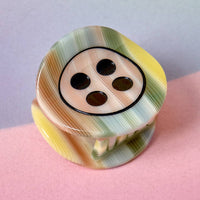 Colorful button-shaped object on a pink surface with a light purple background