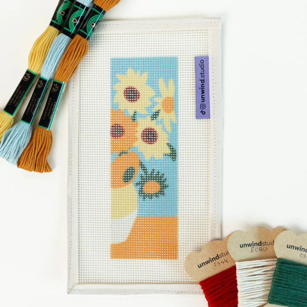Needlepoint kit with sunflower design and embroidery threads on a white background