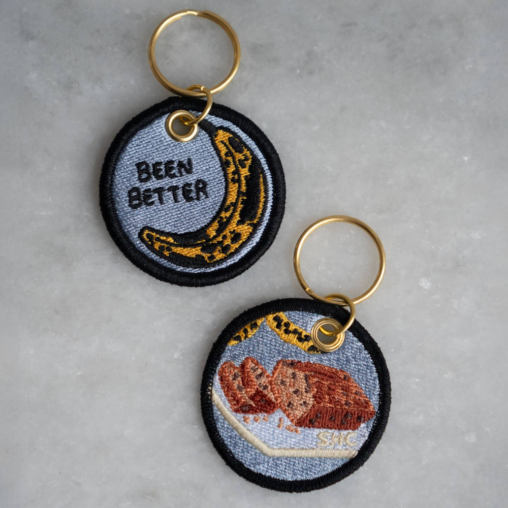 Two sides of an embroidered keychain. One with a banana, saying been better. One with banana bread